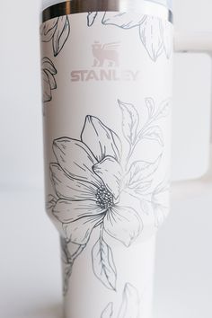 a white coffee cup with flowers painted on the front and sides, sitting on a table