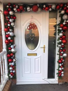 a white door decorated with christmas decorations and ornaments on the front porch, along with red and silver baubes