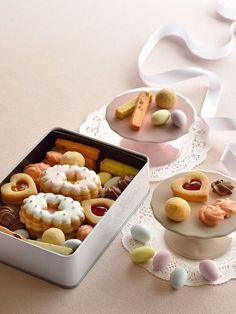 two tins filled with cookies and candies on top of a white doily