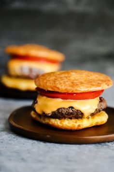 two hamburgers with cheese and tomato on a brown plate next to eachother