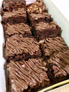 there are many brownies in the box with chocolate icing on them and nuts