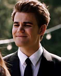 a close up of a person wearing a suit and tie with trees in the background