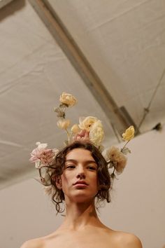 a woman with flowers on her head standing in front of a white wall and ceiling