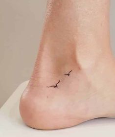 a small black bird tattoo on the side of a person's foot, which is sitting on top of a white table