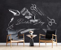 two chairs and a table in front of a chalkboard wall with barbershop drawings on it