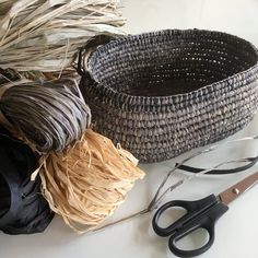 several different types of yarn and scissors on a white table with some grass in the basket