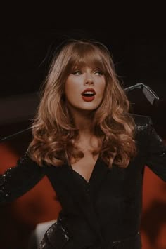 a woman with long hair wearing a black dress and red lipstick on her lips is standing in front of a microphone