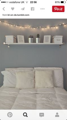 a white bed topped with pillows and blankets under a string of light strung over the headboard