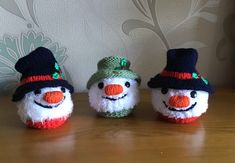 three knitted snowmen with hats and scarves sitting on a wooden table next to a wall