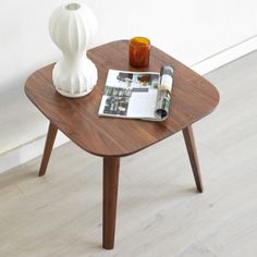 a wooden table with a magazine on it next to a white vase and orange candle