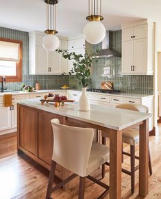 a kitchen with white cabinets and wooden flooring next to an island in the middle