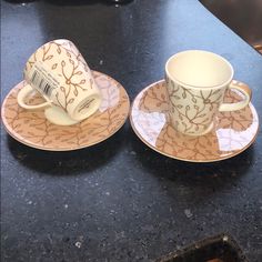 two cups and saucers sitting on top of a black counter next to each other