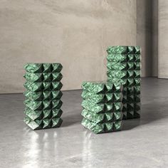 three stacks of green paper stacked on top of each other in front of a concrete wall