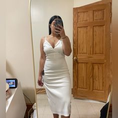 a woman taking a selfie in front of a mirror wearing a white slip dress