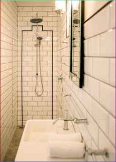 a white tiled bathroom with two sinks and a shower head mounted to the side of the wall