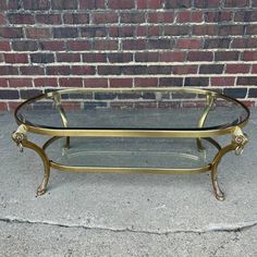 a glass and brass coffee table on concrete with brick wall in the backround