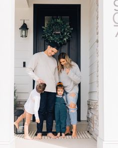 a family standing in front of a door with their two children and one adult looking at the camera