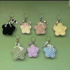 six crocheted keychains are arranged on a green surface, each with a small flower in the center