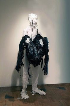 a white and black sculpture with plastic bags on it's back, sitting in front of a wall