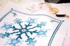 a cross stitched snowflake on a white tablecloth next to a wooden button