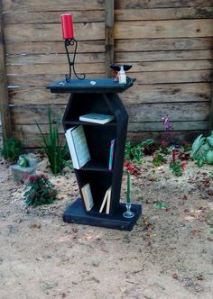 a black book shelf sitting in the middle of a dirt field next to a wooden fence