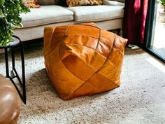 a brown leather pillow sitting on the floor next to a couch and table with potted plants