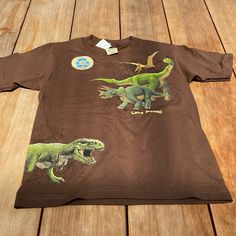 Size 10-12 Brand New Brown Dino Short Sleeve Graphic Tee Cute Brown Tops For Playwear, Summer Dinosaur Print Short Sleeve Tops, Casual Green Dinosaur Print Tops, Casual Green Tops With Dinosaur Print, Casual Cartoon Print T-shirt For Playwear, Casual Character Print T-shirt For Play, Brown Cotton Tops With Cartoon Print, Brown Cotton Top With Cartoon Print, Casual Dinosaur Print Summer Shirt