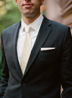 a man in a black suit and white tie is looking at the camera while standing outside