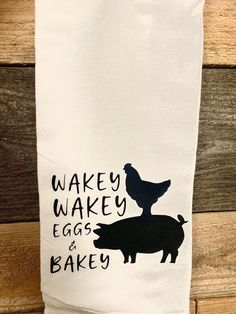 a tea towel with an image of a chicken and a pig on it that says wake wake eggs and bake