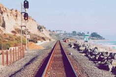 the railroad tracks are lined up next to the beach and cliffs that line the shore