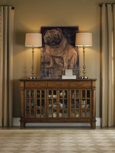 a dog is sitting on top of a wooden cabinet with two lamps next to it