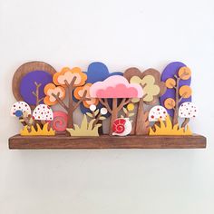 a wooden shelf with various cut out trees and mushrooms on it, along with the number five