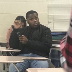 two people sitting at desks with cell phones in their hands and one person looking at his phone