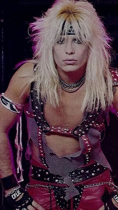 a man with long blonde hair and piercings on his face, dressed in punk clothing