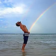 a man standing in the ocean under a rainbow