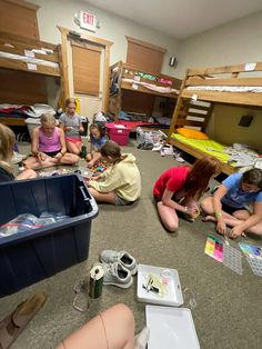 a group of children sitting on the floor in a room with bunk beds and other items