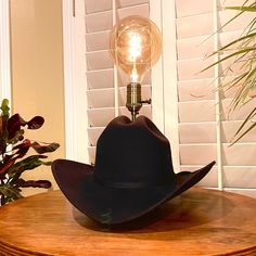 This lamp memorializes that bright idea moment when a lightbulb appears above your head. A high-quality classic felt cowboy hat, this piece will add warm light to a room of any decor. Made with an antique brass dimmable socket with vintage style LED light, 7' rayon wrapped cord, wood base with non-scratch felt furniture pad, and heavy-duty copper and steel parts to hold it all together.  Includes: Lamp Hat, Vintage LED dimmable bulb, Collapsable Felt Carrying Case, and Hat Cleaning Sponge Cowboy Lamp, Black Felt Cowboy Hat, Hat Cleaning, Felt Furniture, Felt Cowboy Hat, Cord Wood, Felt Cowboy Hats, Cleaning Sponge, Lamp Black