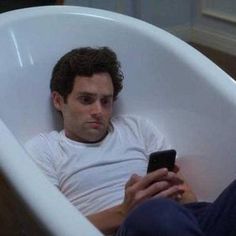 a man sitting in a bathtub holding a cell phone and looking at the screen