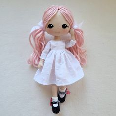 a doll with pink hair and white dress laying down on the floor next to a pair of black shoes