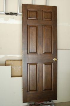 a brown wooden door sitting inside of a room next to a white wall with paint rollers on it