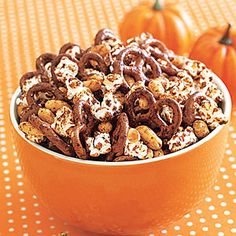 a bowl filled with chocolate covered pretzels on top of a table next to pumpkins