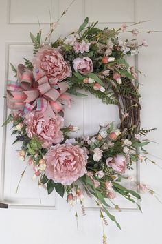 a wreath with pink flowers and greenery hanging on a door