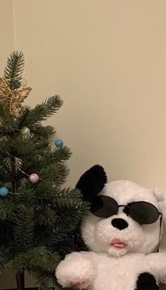 a white teddy bear wearing sunglasses next to a christmas tree