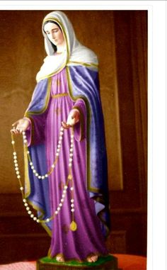 a statue of the virgin mary holding a rosary and wearing a purple dress with gold trimmings