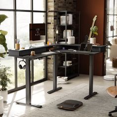 a desk with a laptop on it in front of a window and a potted plant