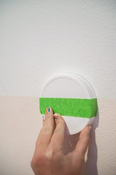 a woman's hand is holding a green and white paper plate on the wall