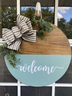 a welcome sign hanging on the side of a door with a bow and greenery