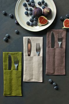 two forks, one knife and some blueberries on a plate next to napkins