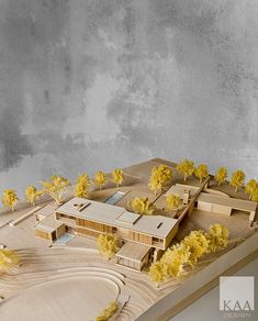 a model of a building with trees in the foreground and yellow flowers on the ground