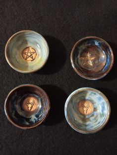 four small bowls with designs on them sitting on a black tableclothed surface and one has a gold star in the center